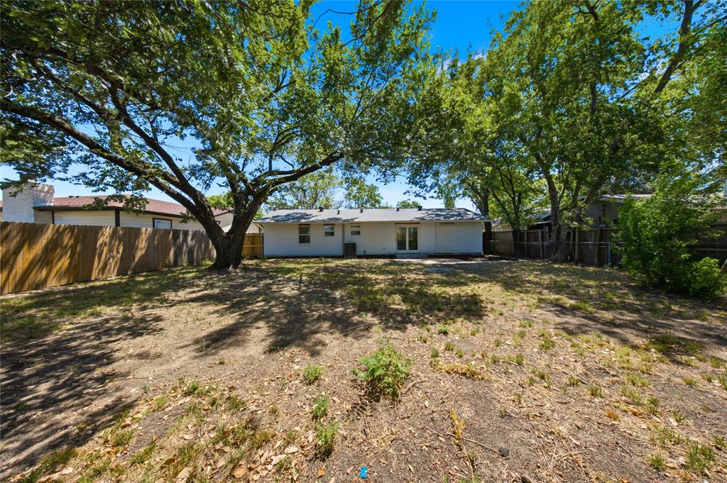 Expansive backyard featuring mature trees, a privacy fence, and a white exterior with a patio area