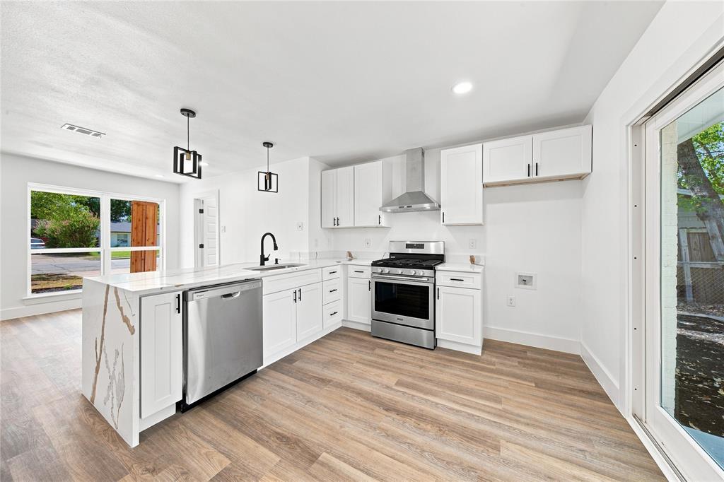 Kitchen featuring a waterfall island, stainless steel appliances, wood-finish flooring, white cabinetry, and pendant lighting
