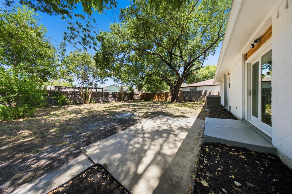 Spacious backyard featuring mature trees, a concrete patio, and a white brick exterior