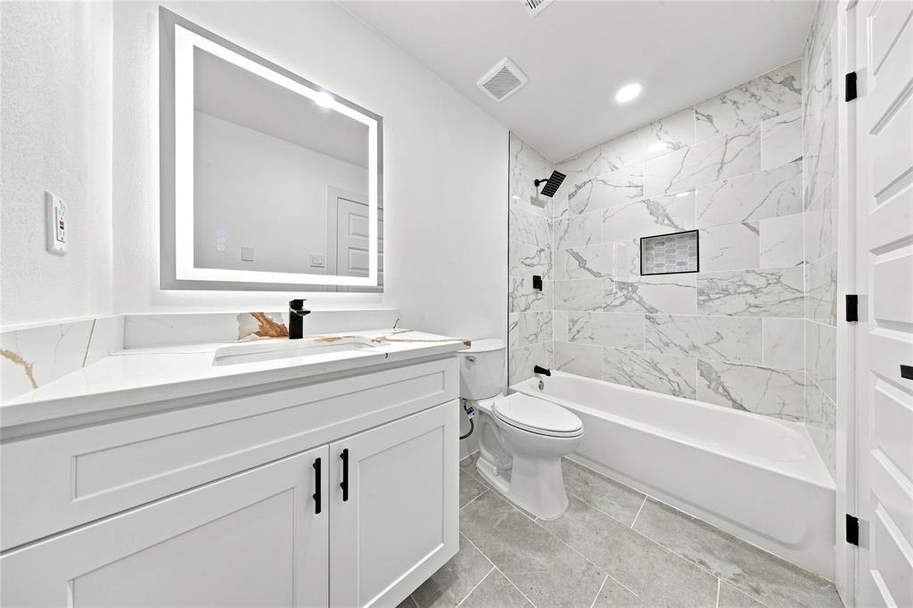 Modern vanity with integrated sink, backlit mirror, matte black fixtures, tiled shower surround, and a built-in shower niche