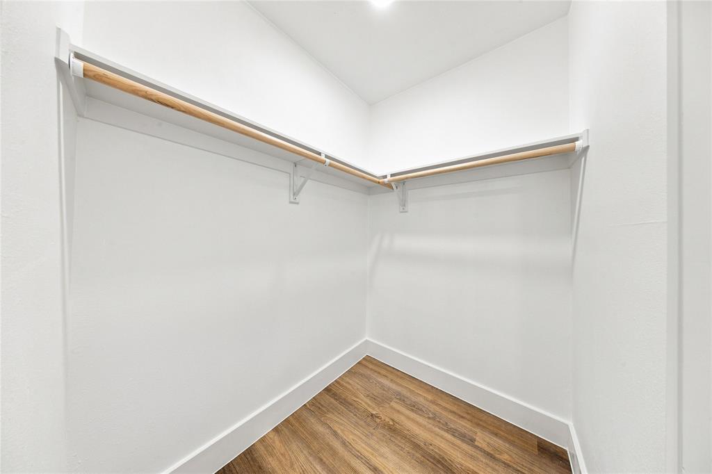 Walk-in closet with wood-finish flooring, white walls, and built-in wood hanging rods