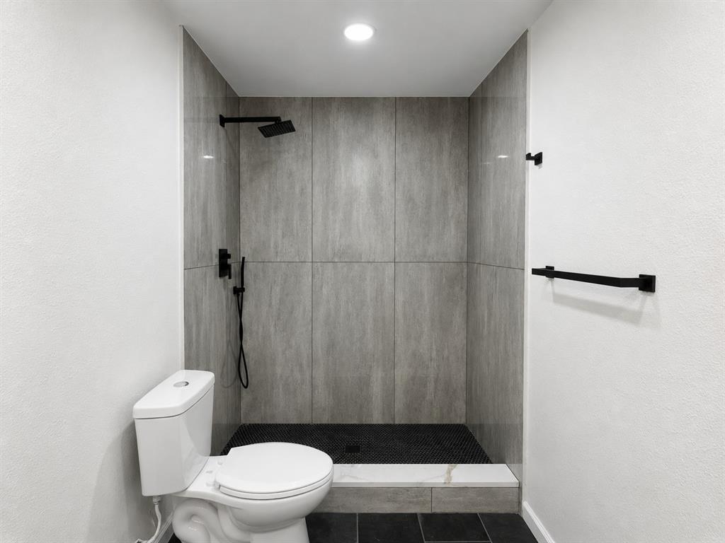 Walk-in shower with large-format wall tiling and dark-toned mosaic floor