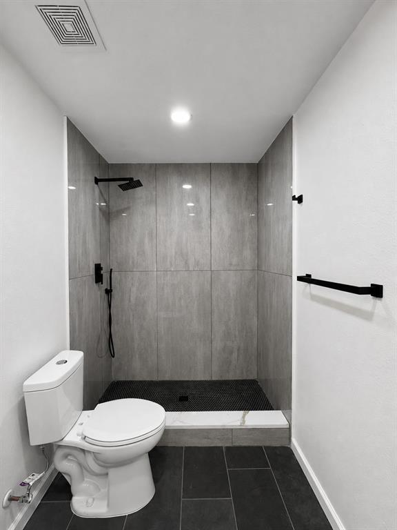 Contemporary walk-in shower with vertical gray wall tiling, black penny tile shower floor, and matte black fixtures