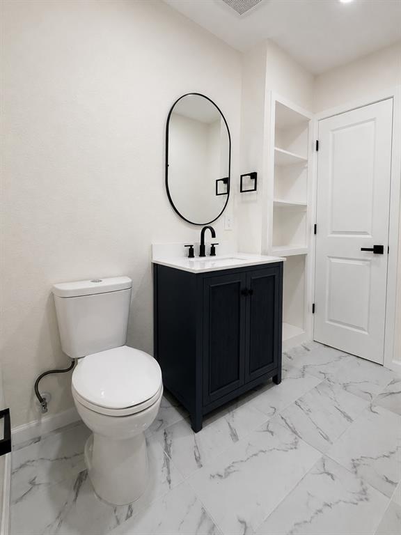 White-veined flooring, vanity with dark cabinetry, modern oval mirror, built-in shelving, and contemporary black fixtures