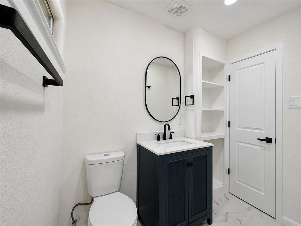 Contemporary bathroom featuring a dark blue vanity with a white countertop, an oval mirror, and built-in shelving