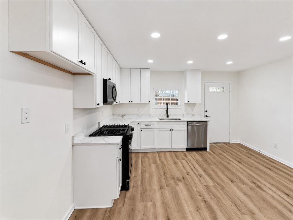 Modern kitchen featuring white cabinetry, light-toned countertops, stainless steel appliances, and wood-finish flooring