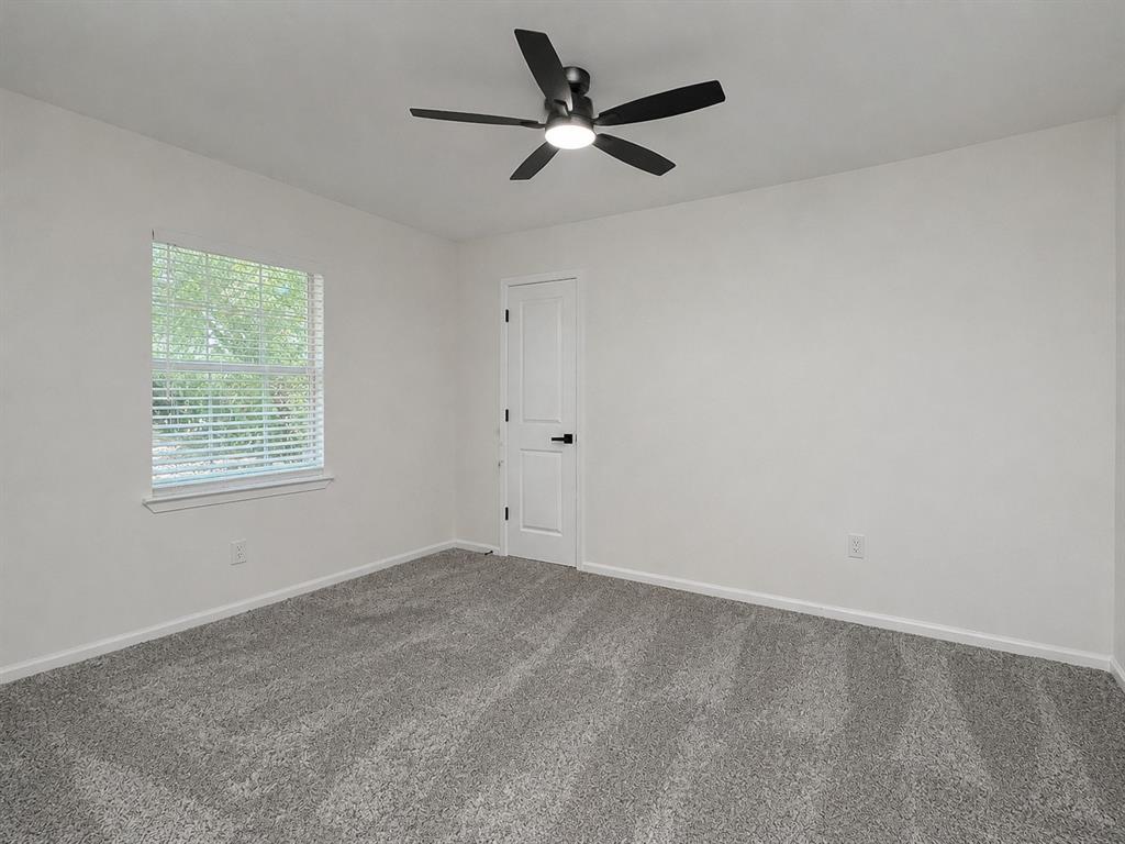 Neutral wall color, grey patterned carpeting, contemporary ceiling fan with light, white door with black hardware, and window with blinds