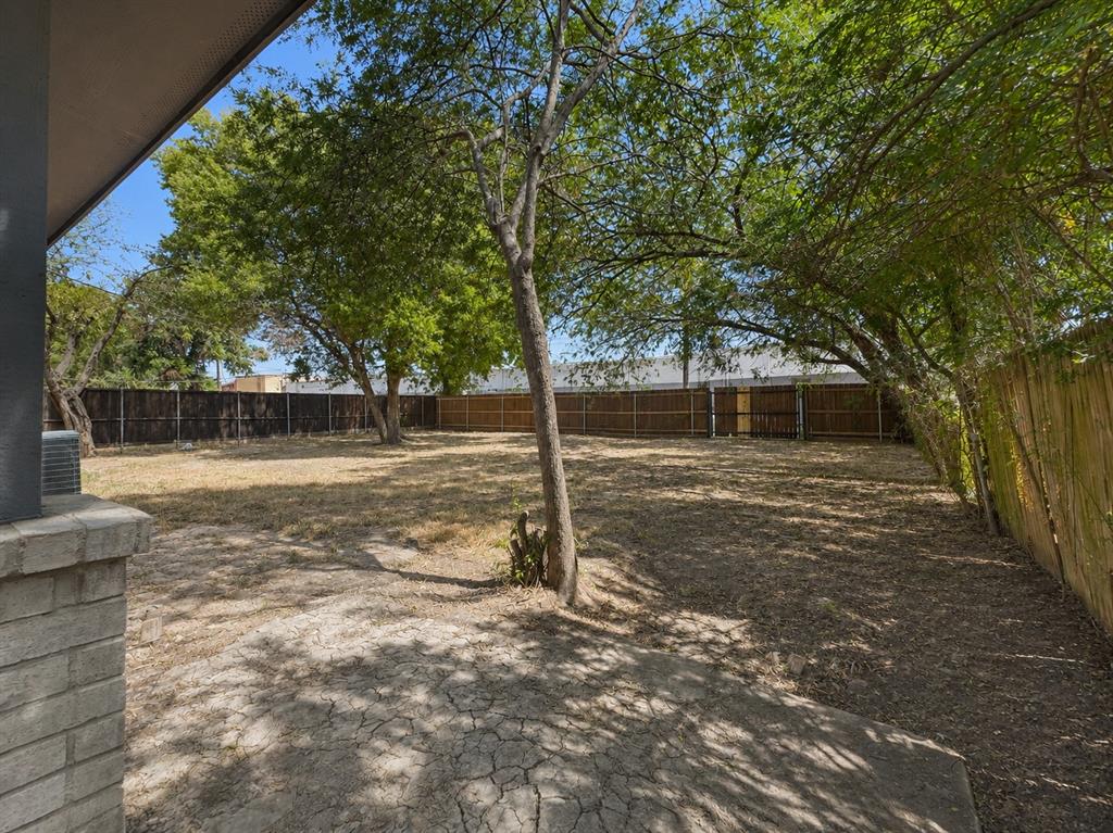 Expansive outdoor space featuring a concrete patio, mature trees, and a full perimeter fence