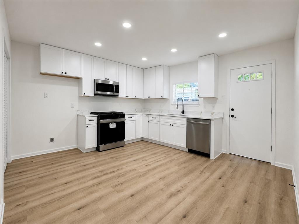 Kitchen featuring white cabinetry, stainless steel appliances, wood-finish flooring, recessed lighting, and a window above the sink