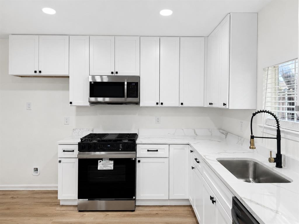 Kitchen featuring white cabinetry, stainless steel appliances, stone countertops, and wood-finish flooring