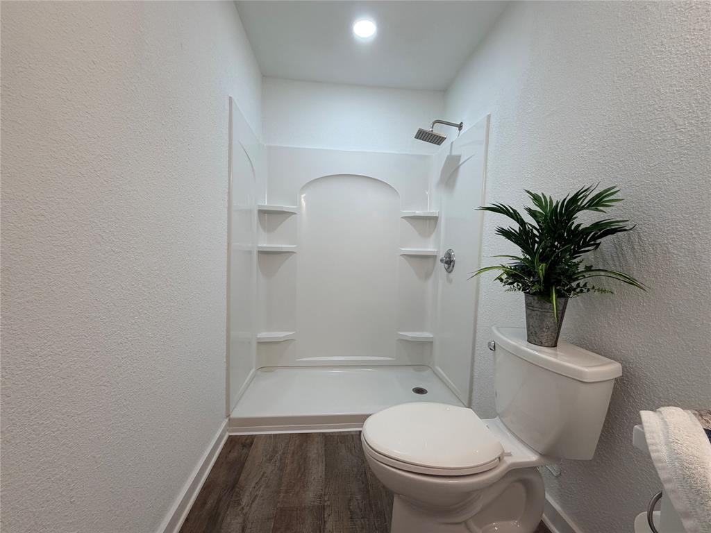 Full shower enclosure with integrated shelving, rainfall showerhead, and wood-finish flooring