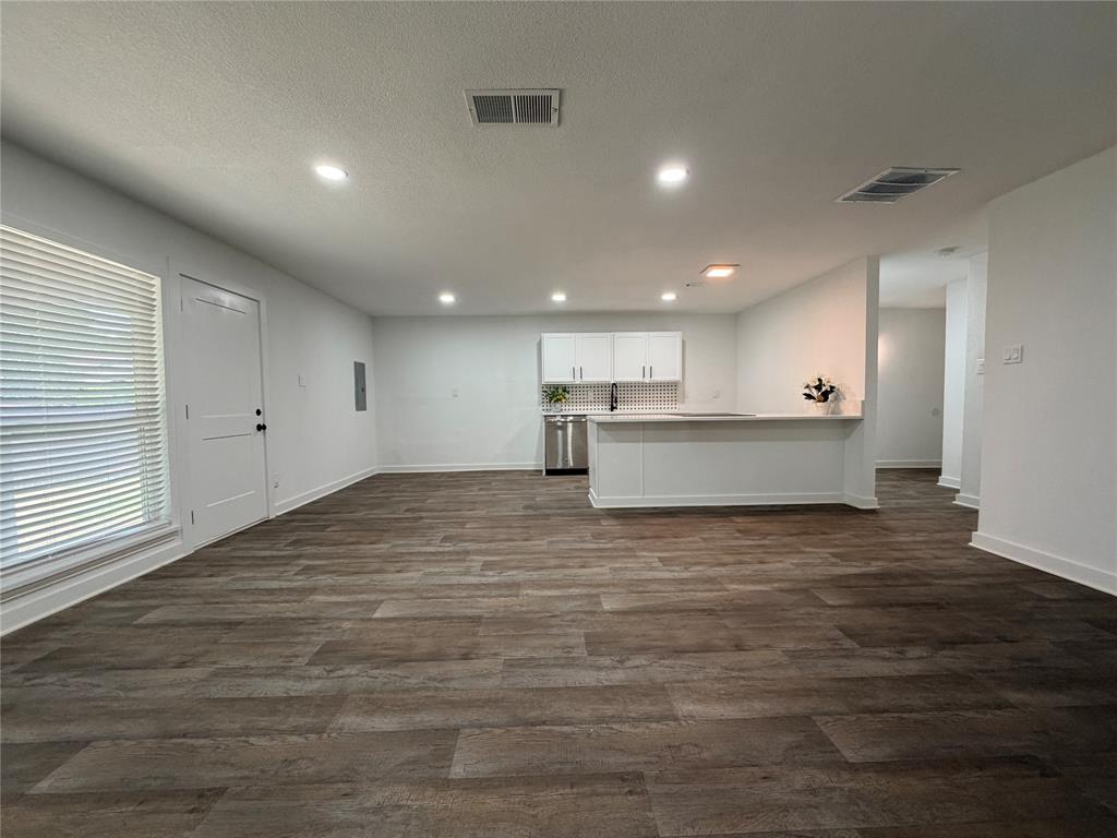 Open-concept living space featuring wood-finish flooring, recessed lighting, and a kitchen with white cabinetry, a tile backsplash, and stainless steel appliances