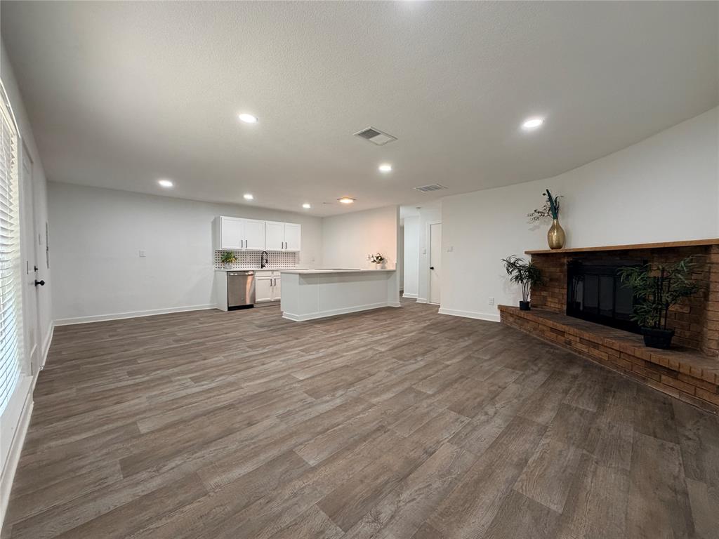 Open-concept living area featuring wood-finish flooring, recessed lighting, and a brick-surround fireplace