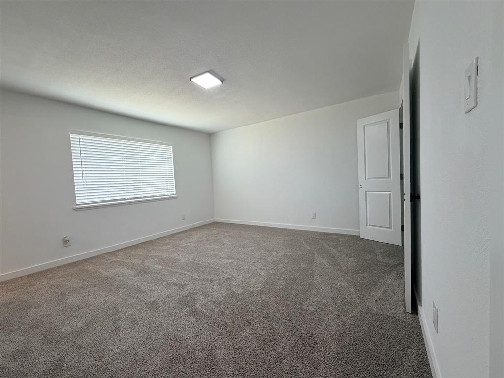 Expansive room featuring neutral-toned carpeting, a window with horizontal blinds, and a flush-mount ceiling light fixture