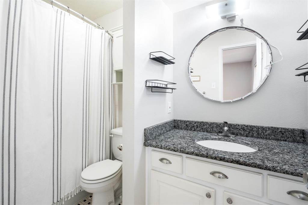White vanity with a granite countertop, integrated sink, and an overhead light fixture