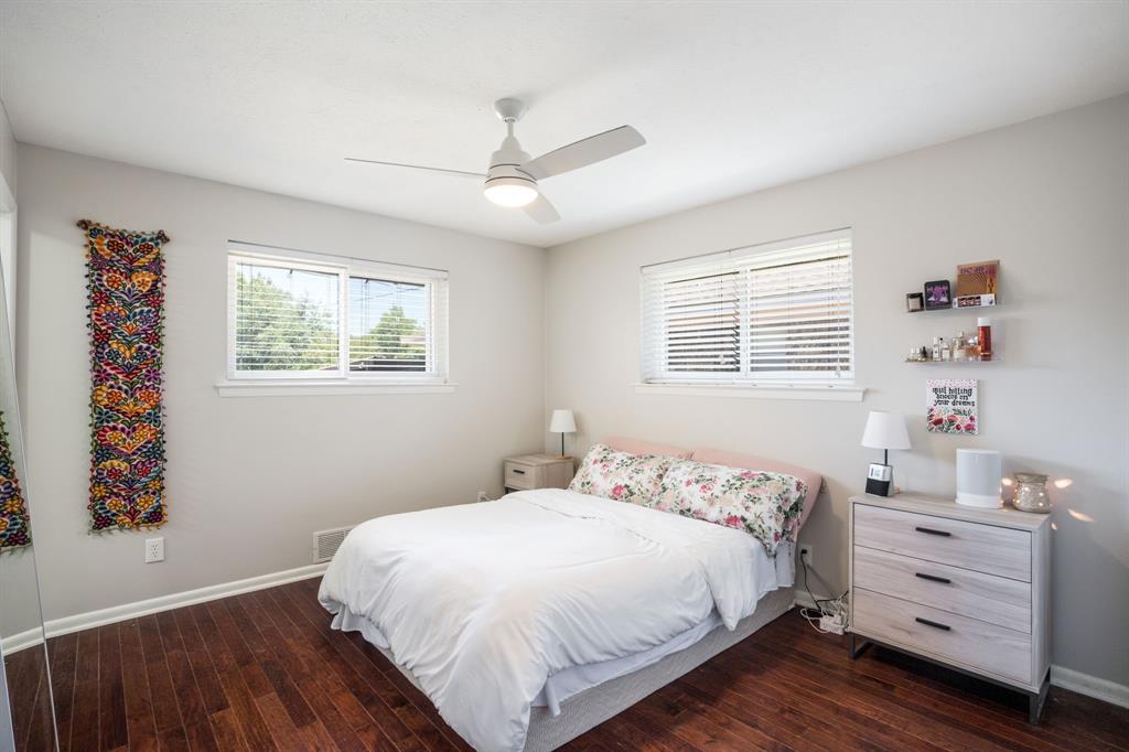 Bright secondary bedroom featuring hardwood flooring, ceiling fan with integrated lighting, dual windows with plantation shutters, and coordinating built-in dresser with three drawers