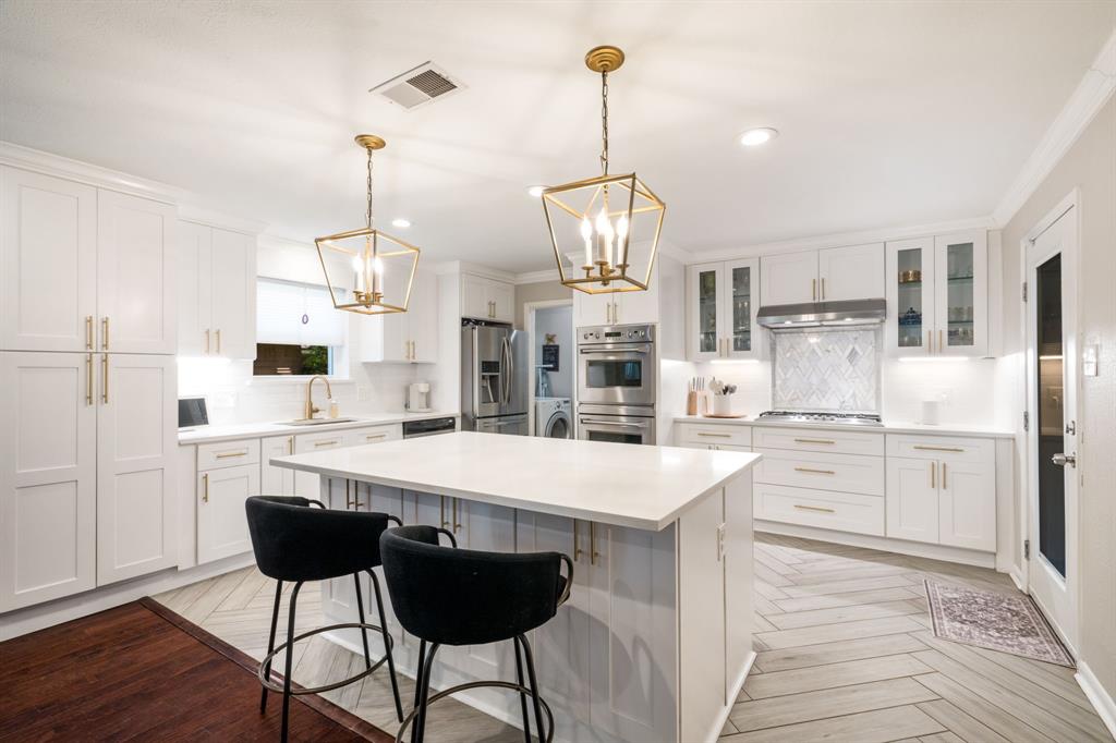 Kitchen with white cabinetry, gold-finish hardware, stainless steel appliances, a center island with a light-toned countertop, and light wood-finish flooring in a herringbone pattern