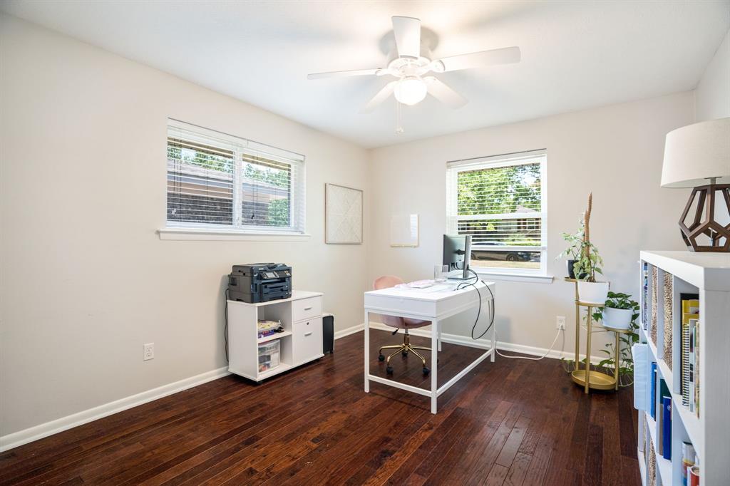 Dark wood-finish flooring, white walls, two windows with blinds, and a ceiling fan with light fixture