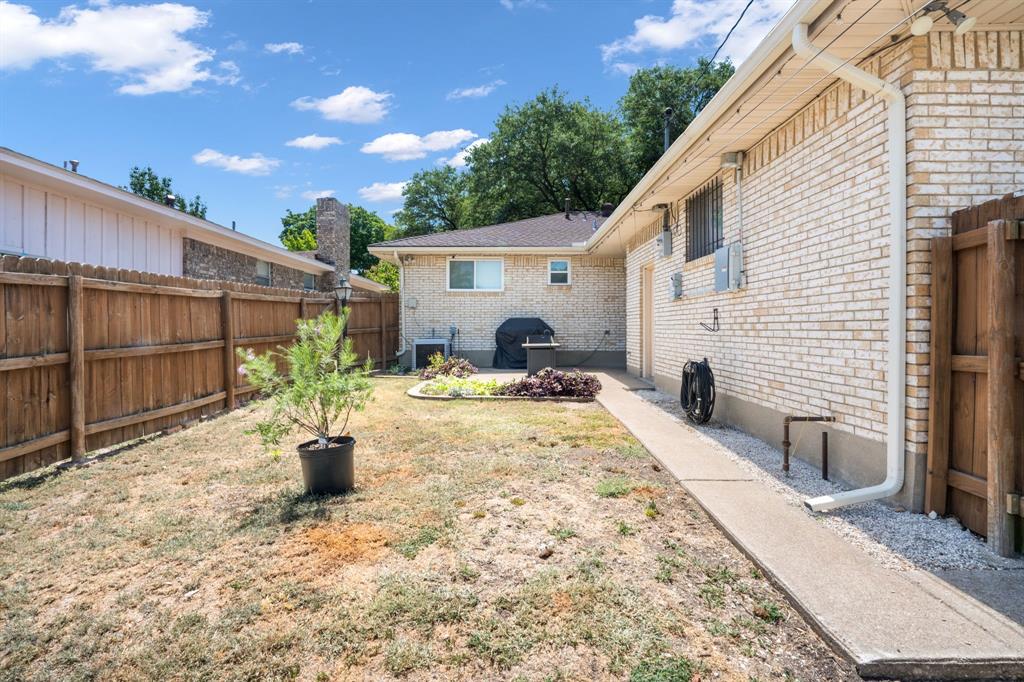 Backyard featuring a privacy fence, concrete walkway, and a brick exterior
