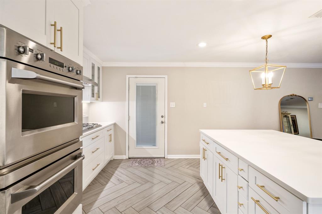 Gourmet kitchen featuring stainless steel double ovens, white cabinetry with brass hardware, and a center island with a solid surface countertop