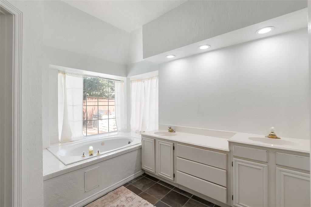 Spacious bathroom with an integrated soaking tub, dual vanity with solid surface countertops, recessed lighting, and dark tile flooring