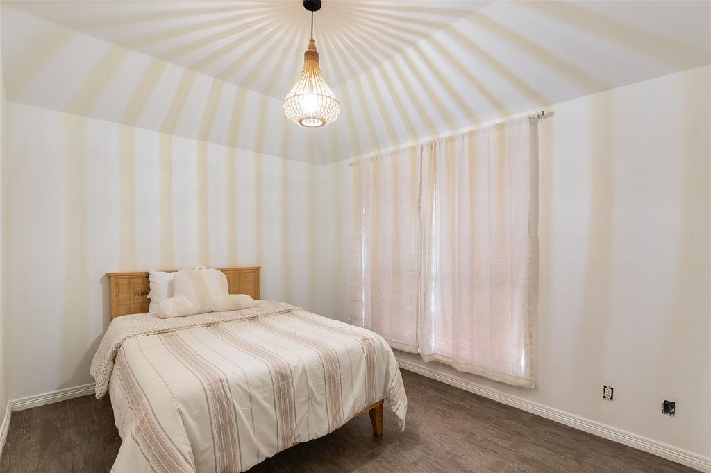 Vaulted ceiling featuring a decorative pendant light fixture, wood-finish flooring, and window with sheer curtains