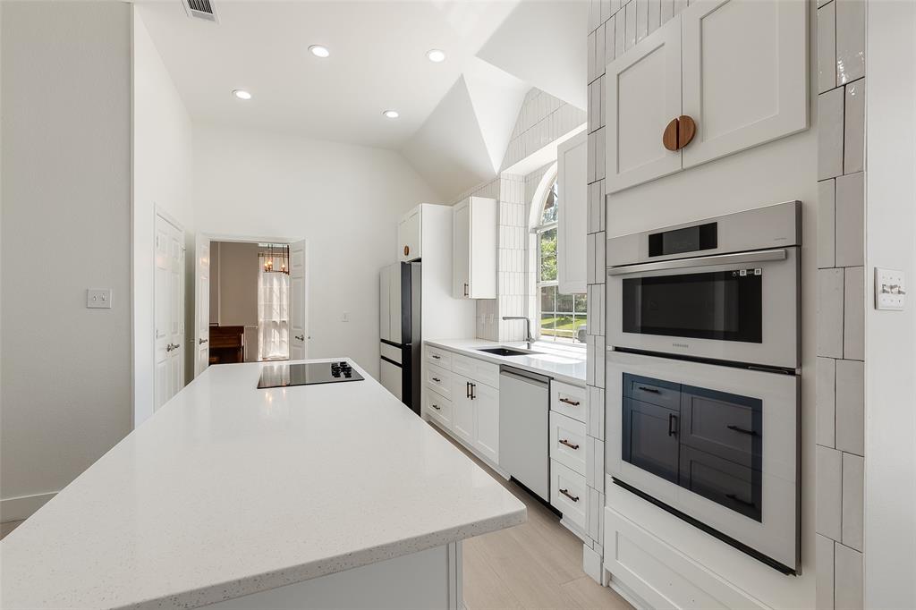 Contemporary kitchen featuring a vaulted ceiling, recessed lighting, white cabinetry, integrated stainless steel appliances, and a central island with a cooktop
