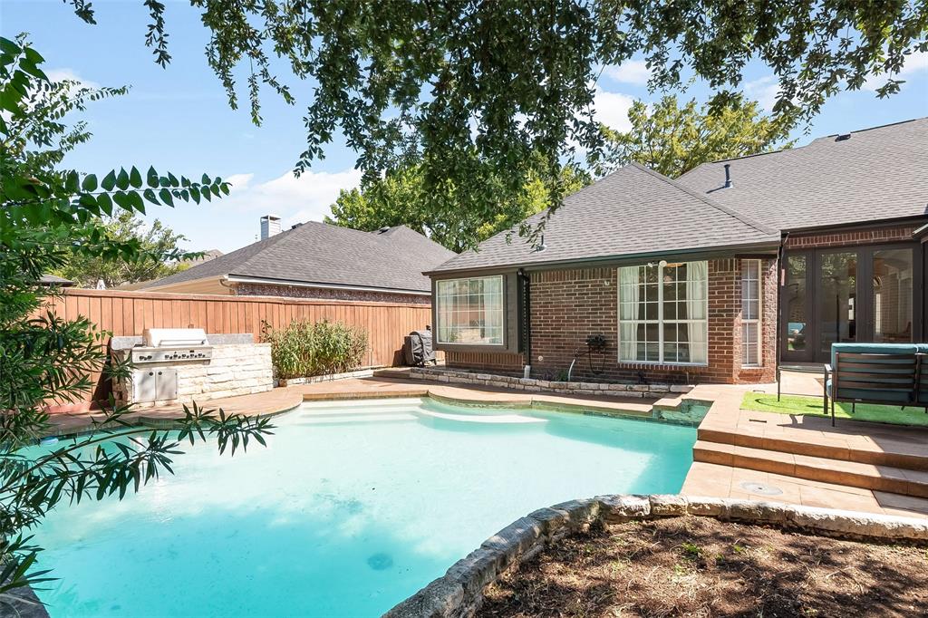 Brick-clad exterior featuring a built-in outdoor grill with stone surround, a multi-level swimming pool, and a private fenced yard