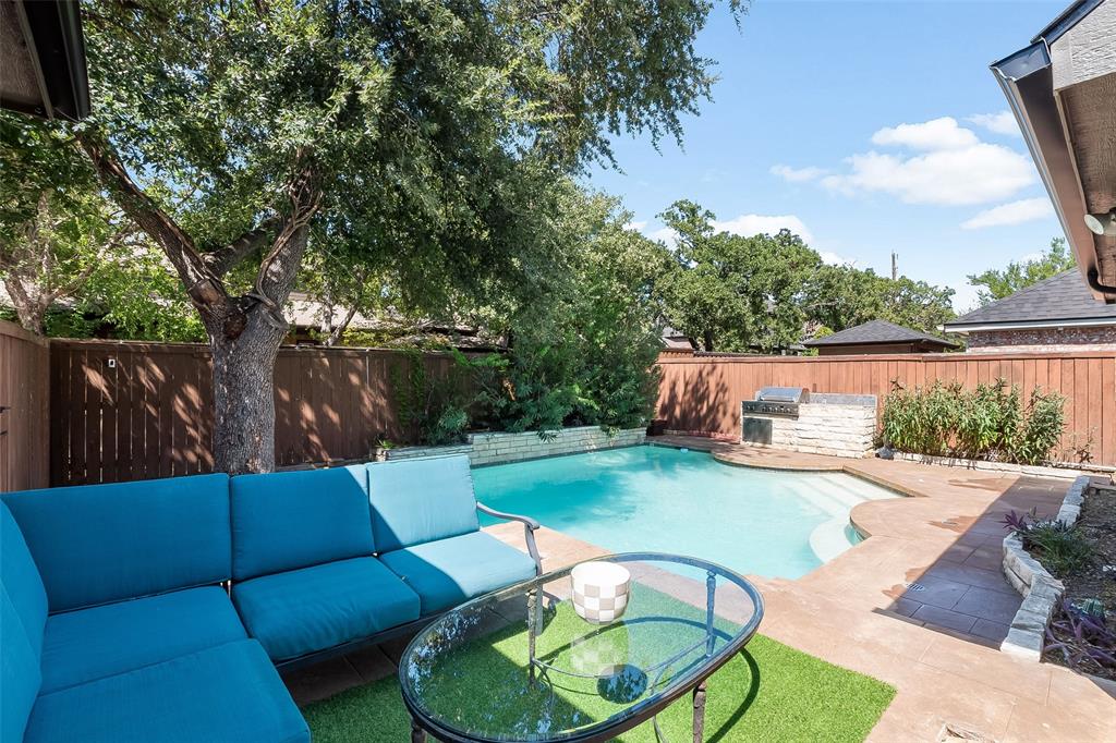 Private backyard featuring a swimming pool, integrated outdoor grill, stone retaining walls, and mature landscaping