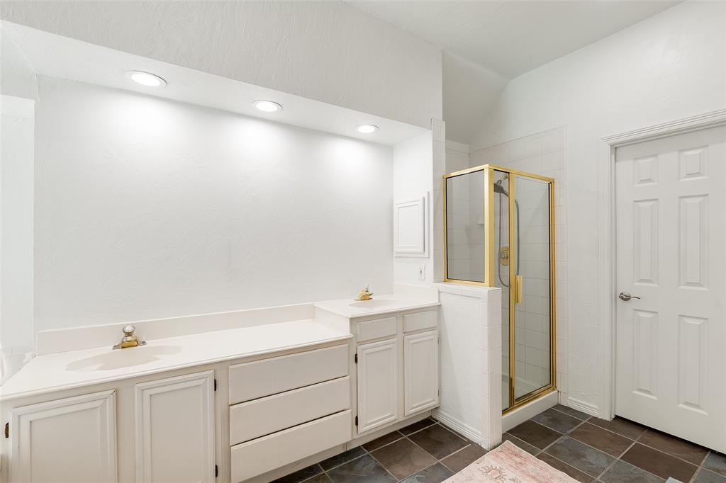 Recessed ceiling lighting, dual vanities with integrated sinks, white cabinetry, gold-framed shower enclosure, and dark square floor tiles
