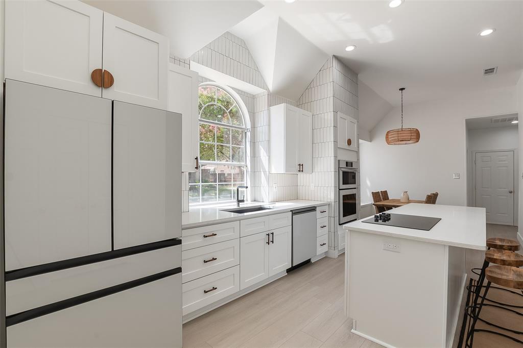Vaulted ceiling, white cabinetry with dark hardware, built-in double oven, built-in cooktop on island, and arched window