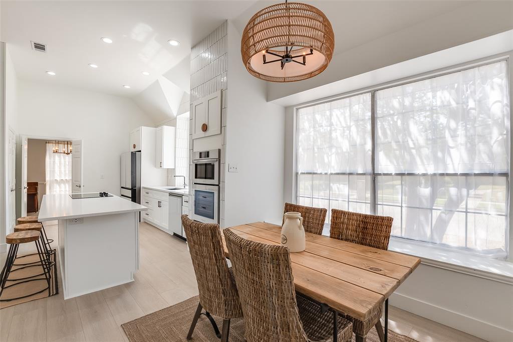 Vaulted ceiling with recessed lighting, integrated double ovens, kitchen island with built-in sink, light wood-finish flooring, and a window with a deep sill