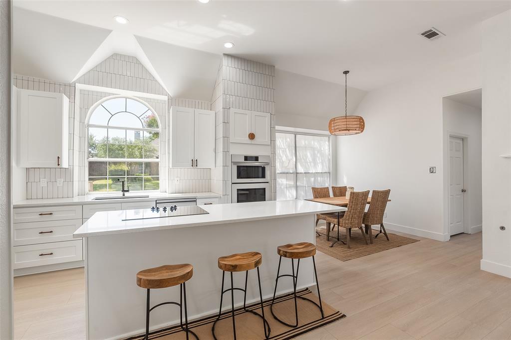 Bright kitchen with vaulted ceiling, arched window, white cabinetry, integrated cooktop, and built-in double oven