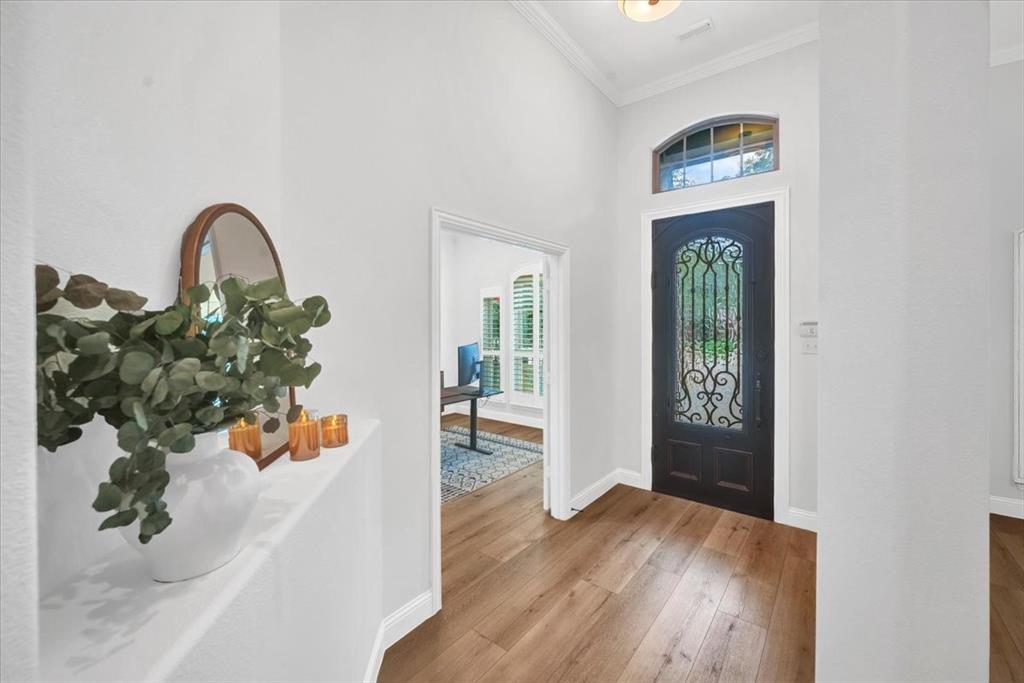 Decorative entry door with wrought iron detailing, arched transom window, wood-finish flooring, and crown molding