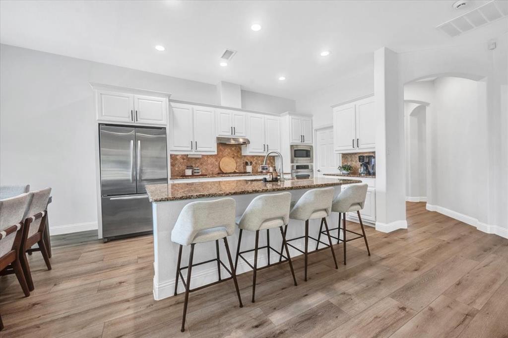 Kitchen featuring wood-finish flooring, white cabinetry, a large kitchen island with counter seating, stainless steel appliances, and recessed lighting