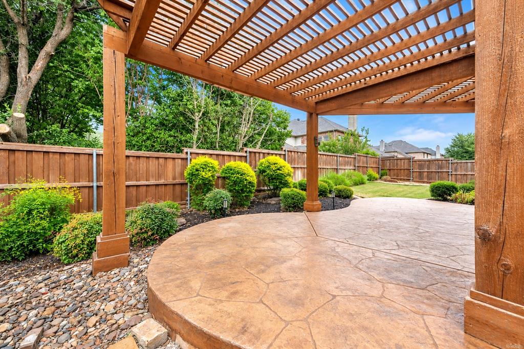Expansive outdoor living area featuring a wooden pergola, stamped concrete patio, manicured lawn, and mature privacy fencing