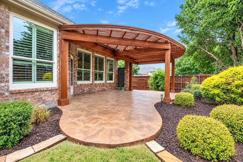 Curved wood pergola over a stamped concrete patio, brick exterior with multiple windows, and landscaped garden beds