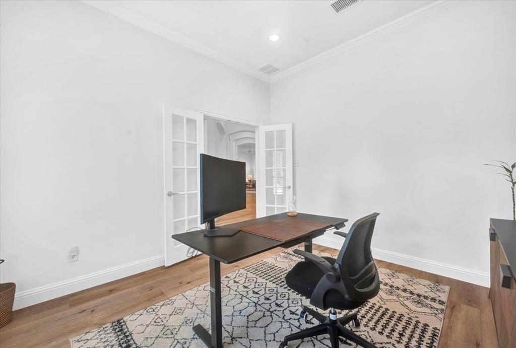 Dedicated home office featuring a wood-finish desk with integrated storage, ergonomic seating, recessed ceiling lighting, and French doors with glass panes opening to adjacent spaces