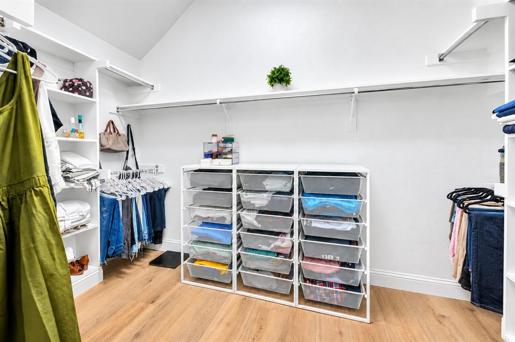 Vaulted ceiling, wood-finish flooring, built-in shelving, white walls, clothes hanging rods