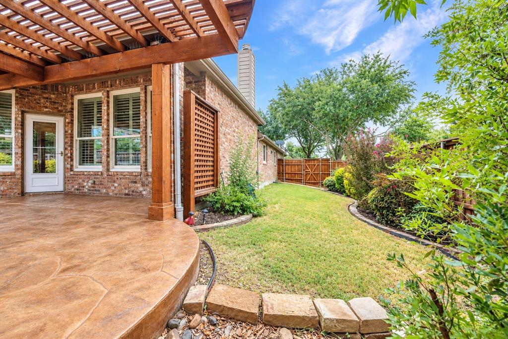 Stained concrete patio with a wooden pergola, brick exterior, and a manicured lawn