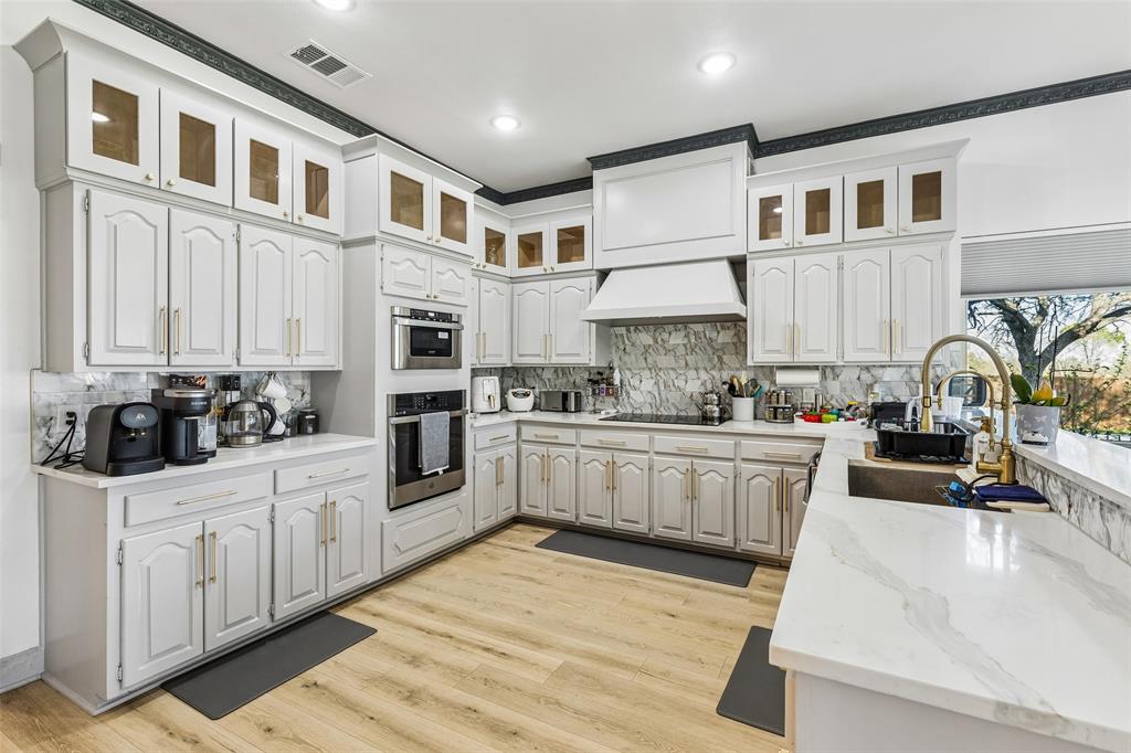 White cabinetry, wood-finish flooring, built-in stainless steel appliances, white countertops, and a full backsplash