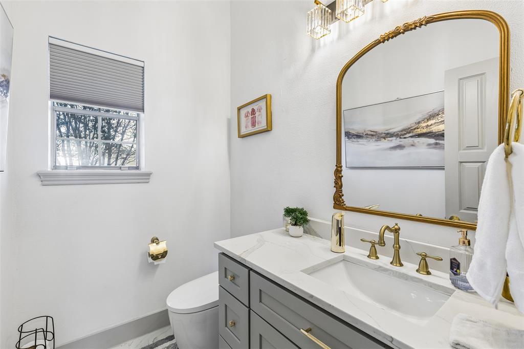Vanity with a white countertop and integrated sink, brass fixtures, decorative framed mirror, and a modern light fixture