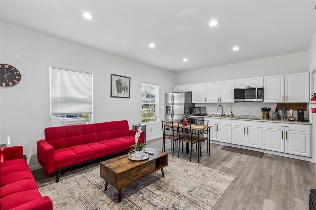 Open-concept living space featuring recessed lighting, light wood-finish flooring, white kitchen cabinetry with gold-tone hardware, and stainless steel appliances