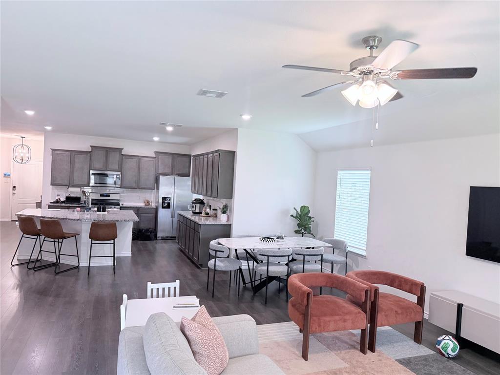 Open-concept living space featuring wood-finish flooring, vaulted ceilings, and a ceiling fan with integrated lighting Open-concept living space featuring wood-finish flooring, vaulted ceilings, and a ceiling fan with integrated lighting