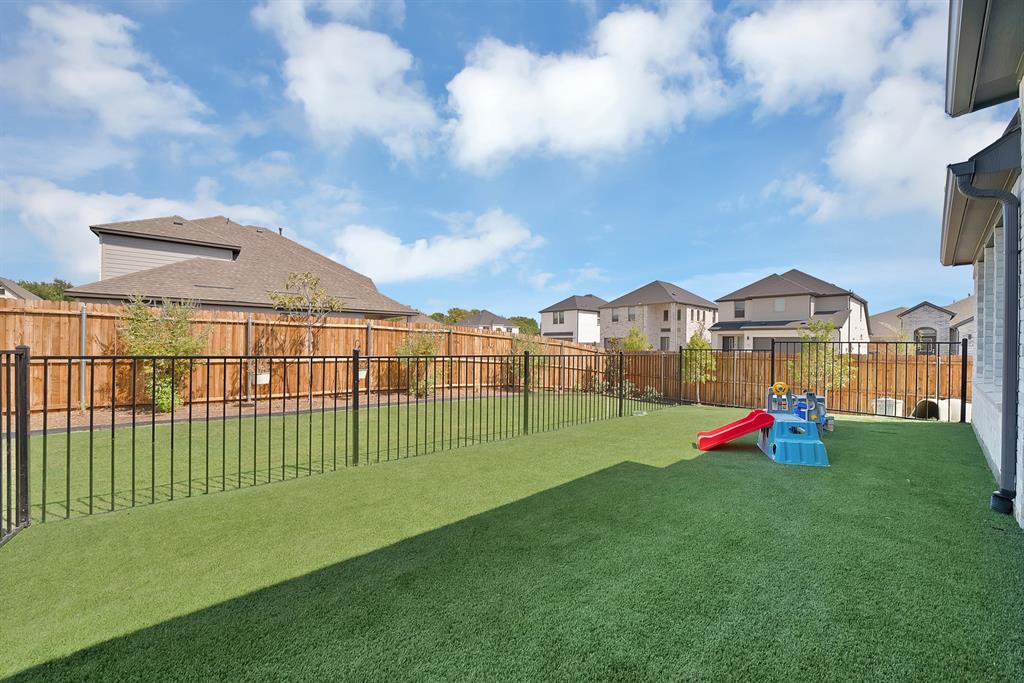 Expansive backyard with professionally installed synthetic turf, black wrought iron perimeter fencing, and dedicated play area.