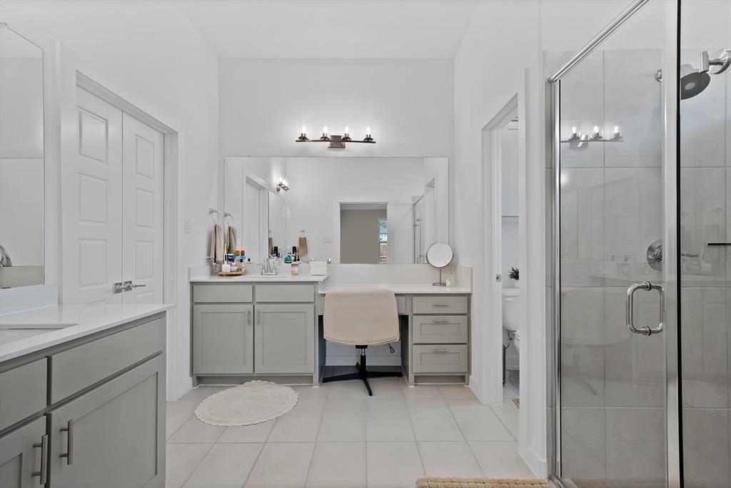 Dual vanity with white countertops and light gray cabinetry, glass-enclosed shower, tiled flooring, and a dedicated vanity seating area.
