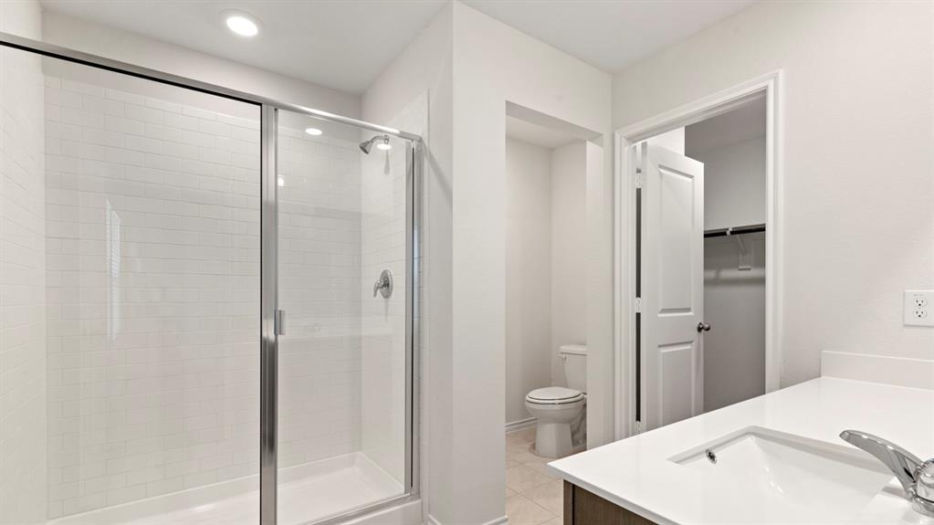 Frameless glass shower enclosure with subway tile surround, white countertop vanity with an integrated sink, and a separate water closet area