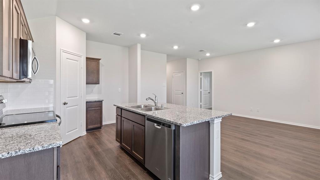 Kitchen featuring an island with a dual-basin sink and stainless steel dishwasher, white subway tile backsplash, granite countertops, and wood-finish flooring