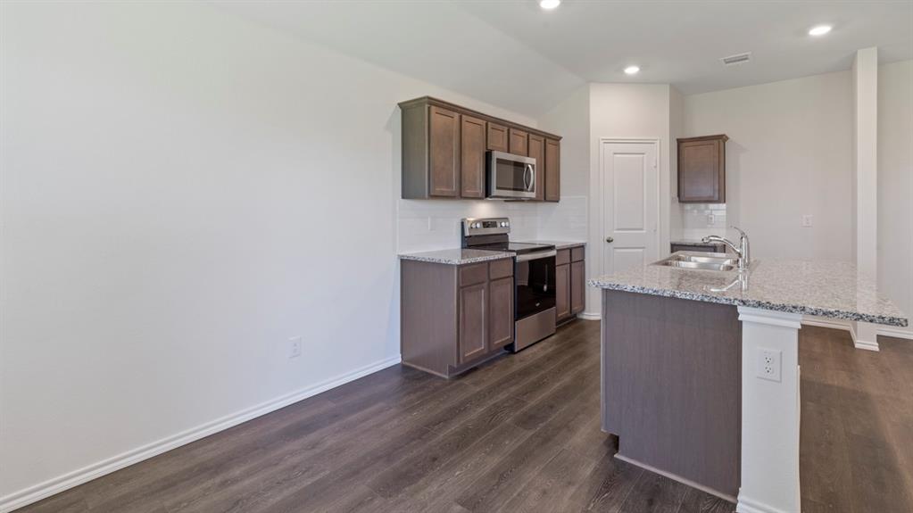 Kitchen featuring wood-finish flooring, recessed lighting, stainless steel appliances, and a central island with a double basin sink and granite countertops