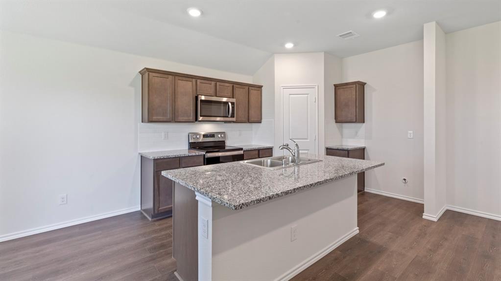 Modern kitchen featuring wood-finish cabinetry, stainless steel appliances, and a spacious granite-topped island with waterfall edge
